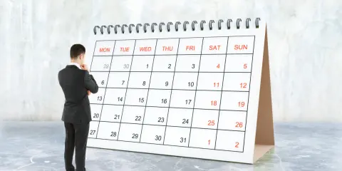 Biznesmen zastanawia się, ile jest dni pracujących w roku, patrząc na kalendarz.