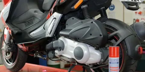 Skuter Gilera z widocznym elementem napędowym. Puszka środka do czyszczenia hamulców obok sugeruje problemy, być może związane z zużytym wariatorem w skuterze objawy.