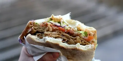 Ręka trzyma pysznego kebaba z mięsem, warzywami i chrupiącą surówką do kebaba.