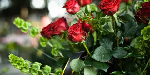 Wieniec pogrzebowy dla brata: bukiet czerwonych róż i zielonych liści, ozdobiony czarną wstęgą ze złotym brzegiem.