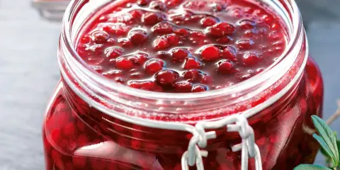 En burk med hemlagad lingonsylt, perfekt för ditt lingonsylt recept. Bären glänser i den söta lagen.