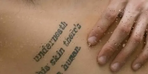 Tatuaż z cytatem "Underneath this skin there's a human" na skórze, z kroplami wody.