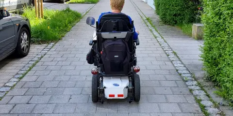 Osoba na wózku elektrycznym porusza się po chodniku. Po udarze, stopień niepełnosprawności może być różny, ale mobilność jest kluczowa.