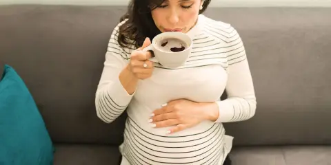 Schwangere Frau trinkt eine Tasse entkoffeinierten Kaffee, während sie ihren Bauch streichelt.