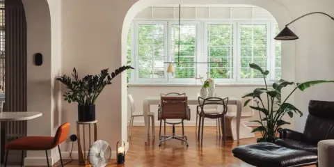 Wnętrze z krzesłem pomarańczowym, wentylatorem i roślinami. To przykład, jak eklektyzm co to znaczy w aranżacji wnętrz, łącząc różne style.