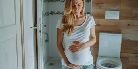 Kobieta w ciąży trzyma się za brzuch, zmartwiona. Czy na początku ciąży boli brzuch jak przy okresie?