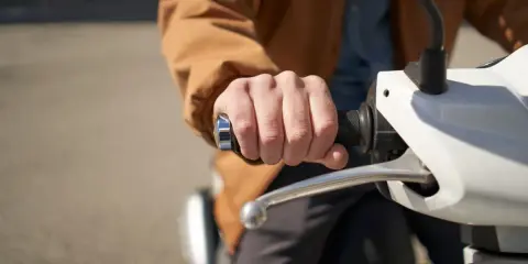 Dłoń trzymająca kierownicę skutera elektrycznego. Może to być związane z dopłatą do skutera elektrycznego.