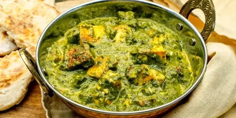 Ein köstliches Palak Paneer in einer traditionellen Schüssel, serviert mit Fladenbrot und Gewürzen.