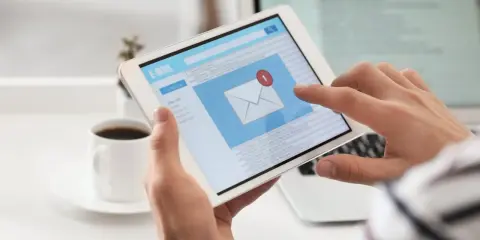 Ręce trzymają tablet z ekranem poczty e-mail, gdzie widać powiadomienie o nowej wiadomości. Może to być początek pisania reklamacji po angielsku.