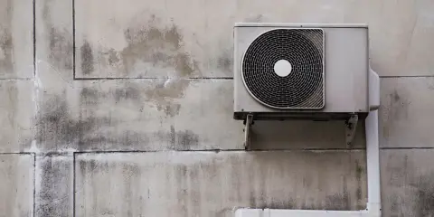 Unité extérieure d'une pompe à chaleur fixée sur un mur en béton. L'isolation est visible sur le tuyau blanc.