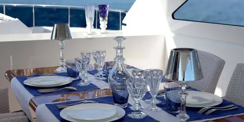 Emplacement des couverts sur une table dressée sur un yacht, avec des verres en cristal, une carafe et des lampes.