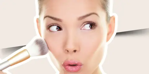 Una mujer aplica colorete en crema en sus mejillas con una brocha, creando un look natural y radiante.
