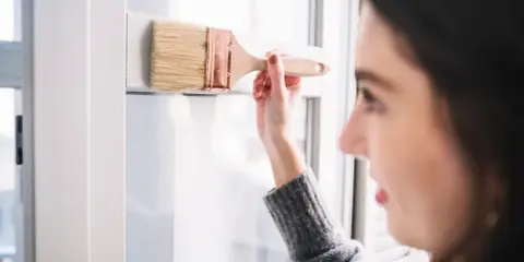 Mujer pintando un marco blanco de PVC con brocha. Aprende como pintar PVC para renovar tus espacios.