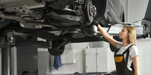 Mechaniczka sprawdza układ napędowy samochodu na podnośniku.