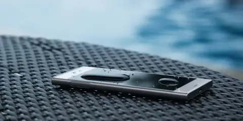Smartfon z kroplami wody na ekranie, leżący na plecionej powierzchni. Dowód, że ip67 co oznacza: odporność na zanurzenie.