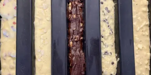 Cinq moules à cake longs prêts pour la cuisson : un aux fruits rouges, un aux amandes, un au chocolat, un aux pépites de chocolat et un aux pommes. Recette 5 cakes longs sucrés.
