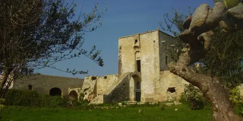 Antica masseria nella pianura salentina, con un torrione in pietra e vegetazione rigogliosa.