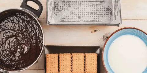 Preparando una deliciosa tarta de galletas y chocolate: chocolate derretido, galletas, molde y leche listos para mezclar.