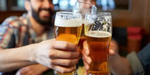 Trzech przyjaciół wznosi toast. Każdy trzyma w dłoni szklankę złocistego piwa z pianką.