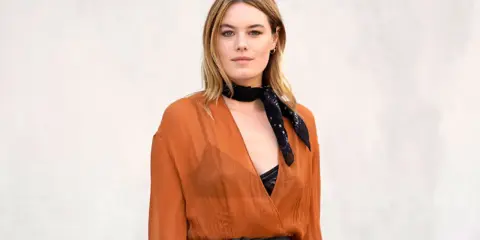 Camille Rowe luce un pañuelo negro y un vestido naranja con escote pronunciado.