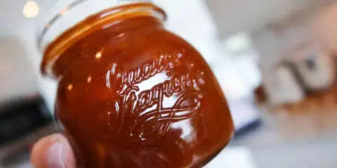 En hand håller ett glas med en mörkröd rabarberchutney. Texten "Quartier" är präglad på glaset.