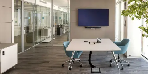 Un bureau futuriste avec une table de réunion, des chaises bleues, un écran mural et des cloisons vitrées.