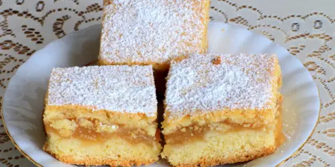 Trzy kawałki biszkoptu z jabłkami, posypane cukrem pudrem, na białym talerzyku.