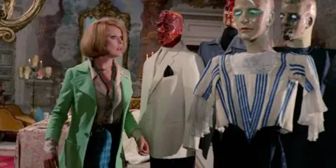 Una donna guarda con terrore manichini inquietanti in un film di Mario Bava.