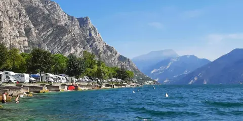 Malowniczy pole namiotowe Garda nad jeziorem, z kamperami i górami w tle.