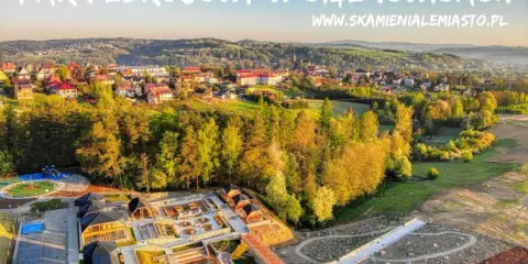 Widok z lotu ptaka na park zdrojowy w Ciężkowicach z placem zabaw, basenem i drewnianymi altanami.