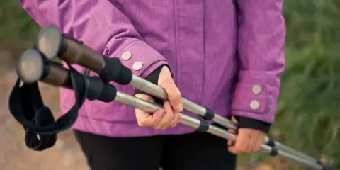 Osoba w fioletowej kurtce trzyma kijki trekkingowe. Zastanawiasz się nad przeciwwskazaniami do chodzenia z kijkami?
