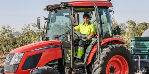 Un homme souriant conduit un tracteur rouge, une machine pour arracher des bambous, prêt à travailler dans un champ.