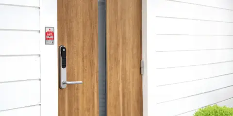 En modern ytterdörr med ett Yale Doorman Classic vs V2N lås. Dörren är i trä och husfasaden är vit.