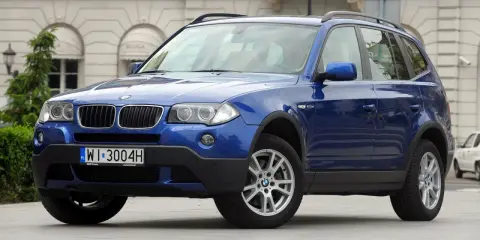 Niebieskie BMW E83, SUV, stoi przed budynkiem z łukami.