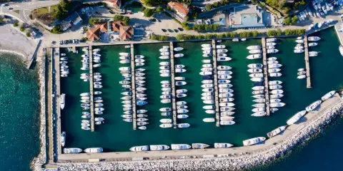 Widok z lotu ptaka na port w Chorwacji, pełen białych jachtów i łodzi zacumowanych w turkusowej wodzie.