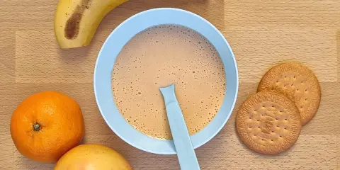 Un tazón de papilla galletas maría con frutas: plátano, naranja y manzana.