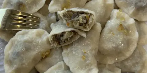 Talerz pełen pysznych, domowych pierogów z kapustą i grzybami. Jeden pieróg jest przekrojony, ukazując bogate nadzienie. Obok leży złoty widelec.