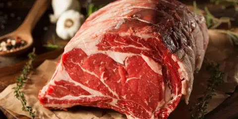 Un succulento pezzo di carne cruda, pronto per diventare un delizioso brasato di manzo. Spezie, erbe aromatiche e aglio completano la scena.