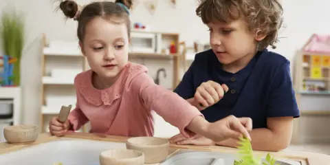 Dwoje dzieci bawi się w piaskownicy sensorycznej z niebieskim piaskiem i roślinami.
