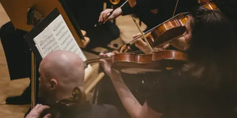Skupieni muzycy grają na skrzypcach podczas części koncertu bez solisty. Nutki na pulpicie wskazują melodię.