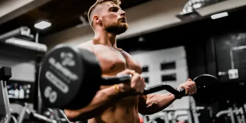 Mężczyzna ćwiczy biceps z ciężarem, wiedząc, że shake proteinowy co daje dla mięśni.