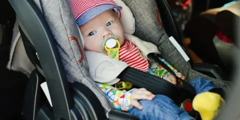 Baby mit Schnuller in Babyschale. Wann wechseln von Babyschale auf Kindersitz? Das Baby ist bereit für den nächsten Schritt.