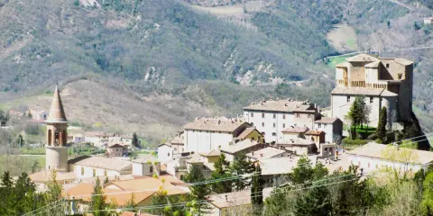 Borgo medievale con torre campanaria e rocca imponente, immerso tra le colline verdi. Un angolo di storia vicino a Marecchia Rimini.