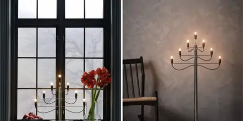 Två fina adventsljusstakar, en i ett mörkt fönster med amaryllis och äpplen, en annan som golvlampa bredvid en gungstol.