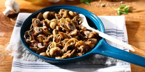 Aksamitne, duszony pieczarki z cebulką w niebieskiej patelni, gotowe do podania.