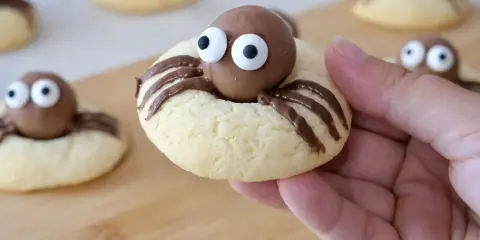 Des cookies araignée adorables avec des yeux en sucre et des pattes en chocolat, prêts à être dégustés.