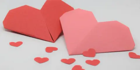 Zwei Origami-Herzen, rot und rosa, umgeben von kleinen roten Herzen. Perfekt zum **Herzen basteln** für den Valentinstag.