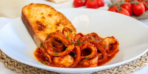 Moscardini in umido, teneri e saporiti, serviti con pane tostato e pomodorini freschi.
