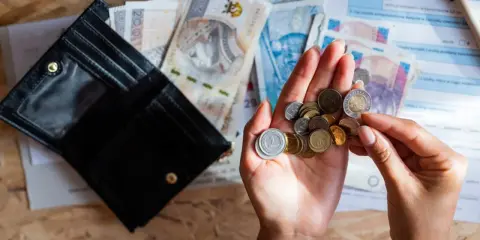 Otwarty portfel, polskie banknoty i monety w dłoni na tle dokumentów.