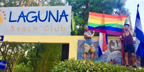 Two men proudly hold a rainbow flag at Laguna Beach Club, celebrating gay pride in Guatemala.